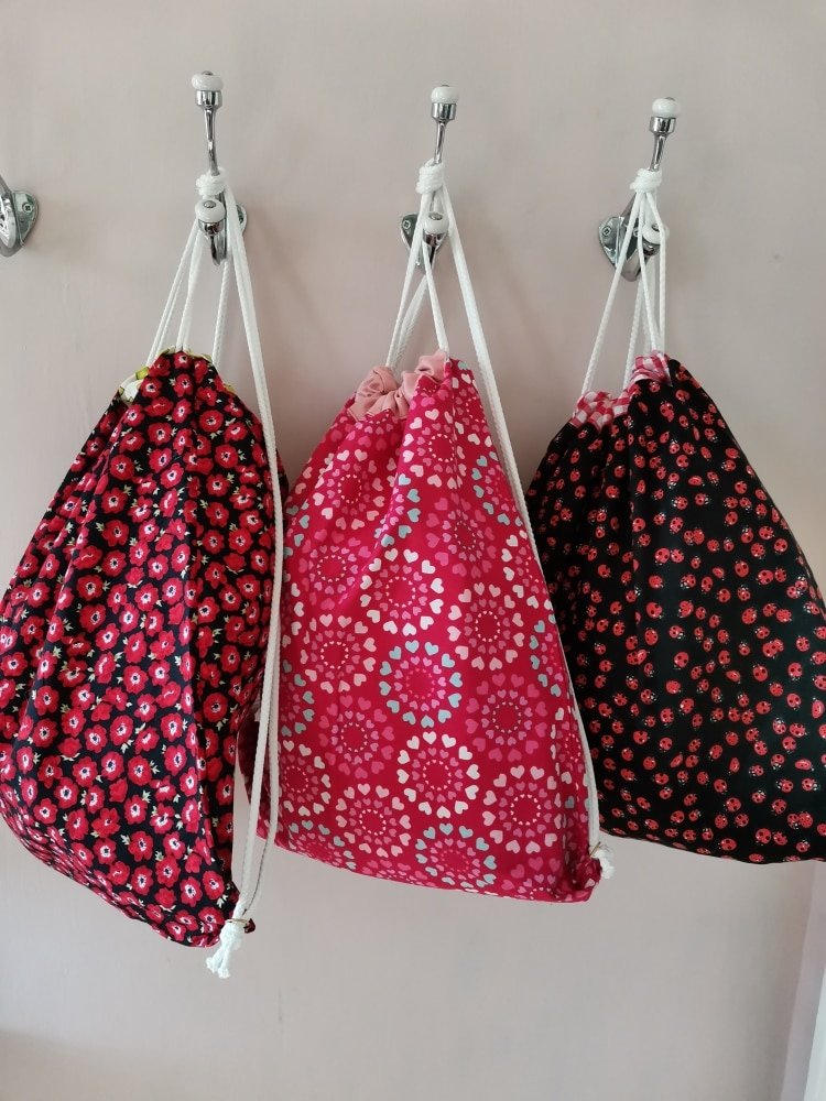 Three drawstring bags (back packs) hanging from hooks